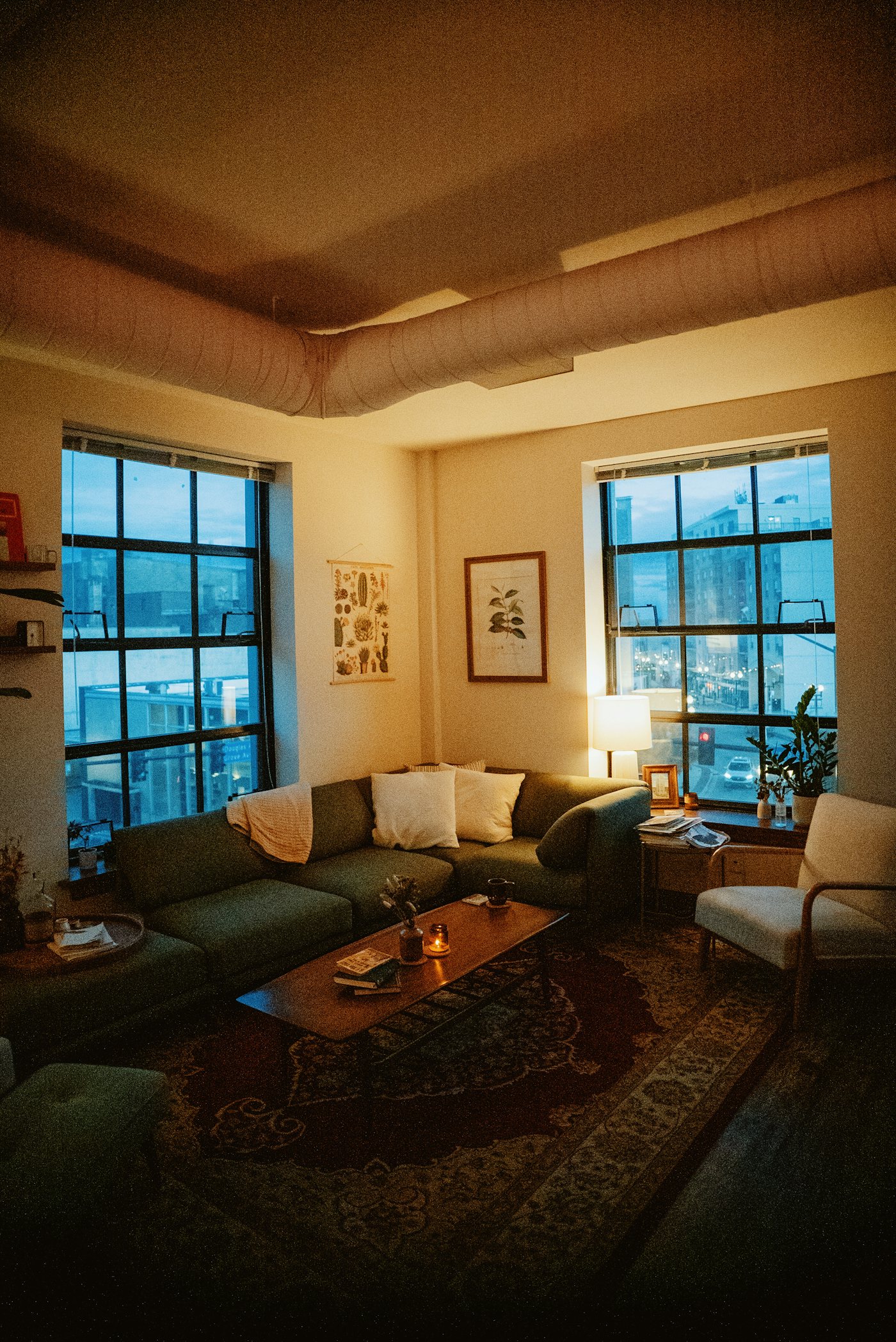 Wohnzimmer am Abend mit warmem Licht, Sofa und Sprossenfenstern